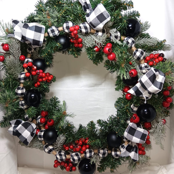 Decorative Christmas wreath with black and white checkered ribbons, red berries, black ornaments, and greenery.